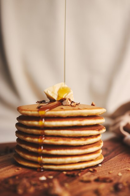 Vertikale Aufnahme von Pfannkuchen mit Sirup, Butter und gerösteten Nüssen auf einem Holzteller