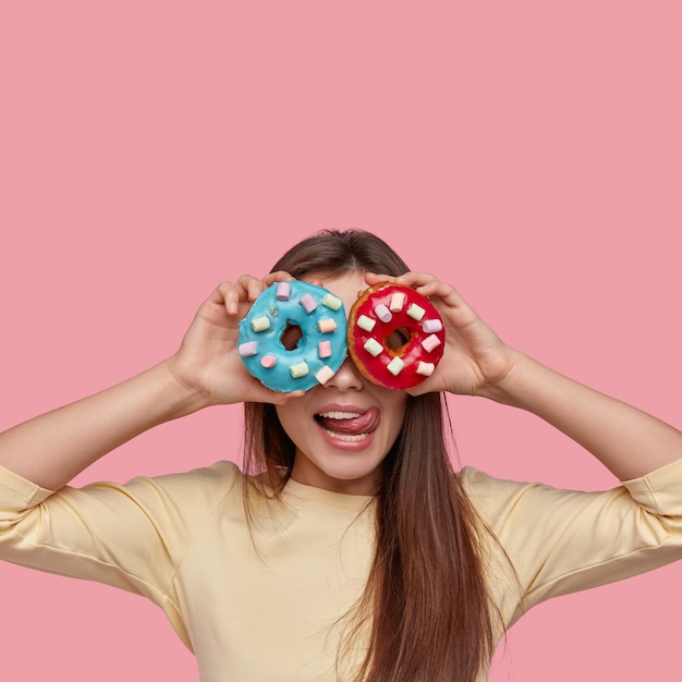 Vertikale Aufnahme von schönen Dame bedeckt Augen hat zwei blaue und rote Donuts