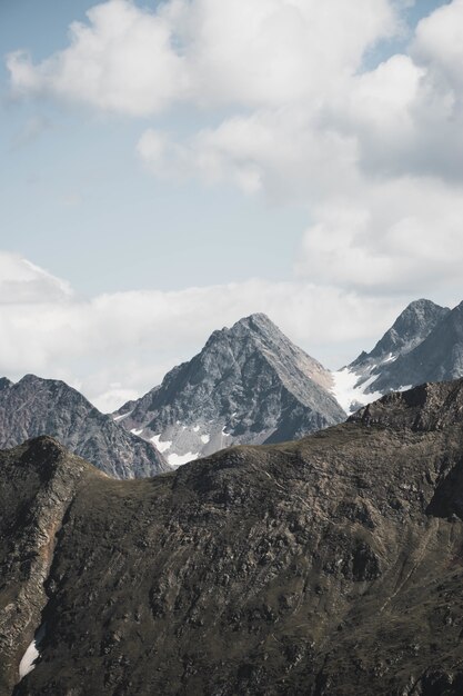 Vertikale Aufnahme von schönen schneebedeckten Bergen unter atemberaubenden Wolken im hellblauen Himmel