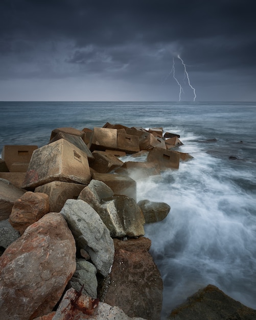 Kostenloses Foto vertikale aufnahme von steinen im meer während eines gewitters und eines blitzes