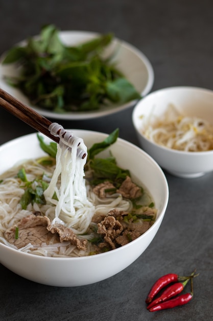 Vertikale Aufnahme von vietnamesischem Essen, Pho Bo Suppe mit roten Chilis auf dem Tisch