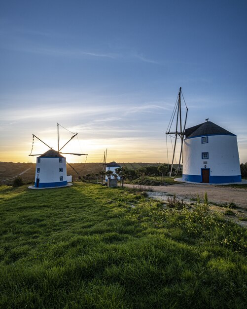 Vertikale Aufnahme von Windmühlen mit einem Sonnenaufgang in einem klaren blauen Himmel im Hintergrund