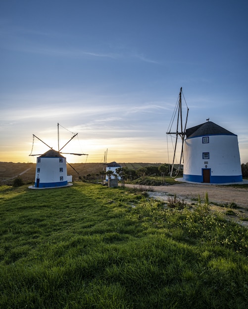 Vertikale Aufnahme von Windmühlen mit einem Sonnenaufgang in einem klaren blauen Himmel im Hintergrund