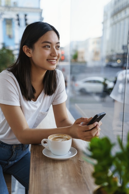 Vertikale Außenaufnahme fröhliche schöne junge moderne asiatische Mädchen im T-Shirt, Jeans, magerer Couchtisch.