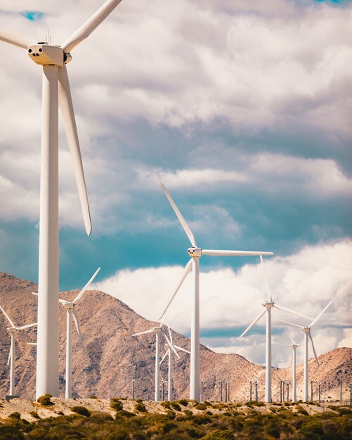 Vertikale Flachwinkelaufnahme von vielen Windmühlen in einem Feld, das von hohen felsigen Bergen umgeben ist