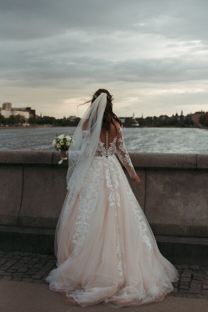 Vertikale Ganzkörperaufnahme einer Braut, die weißes Kleid und Hochzeitskleid trägt, die auf einer Brücke stehen