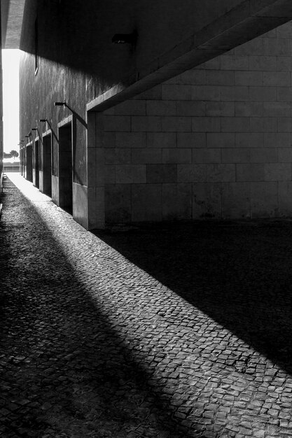 Vertikale Graustufenaufnahme der Sonne, die auf dem Bürgersteig durch die Gebäude scheint