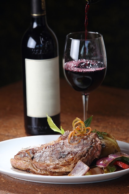 Kostenloses Foto vertikale nahaufnahme eines frisch gegrillten t-bone-steaks und eines glases wein im hintergrund