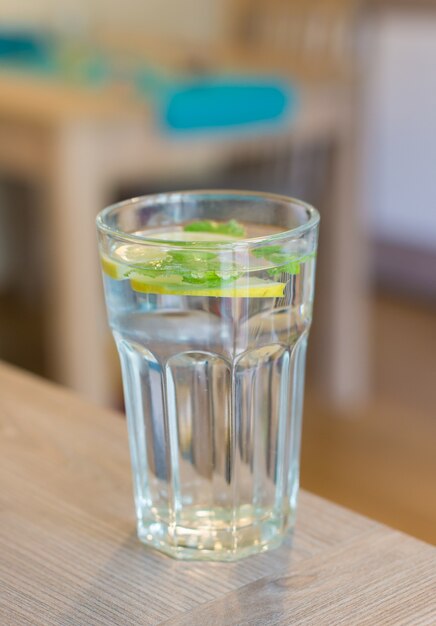 Vertikale Nahaufnahme eines Glases Wasser mit Zitrone und Minze mit einem unscharfen Raum