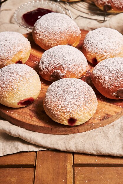 Vertikale Nahaufnahme von flauschigen Donuts gefüllt mit Marmelade auf einem Tablett auf dem Tisch unter den Lichtern