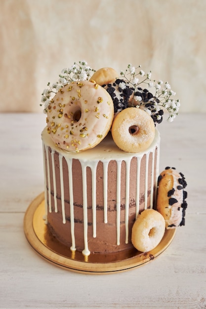 Vertikale nahaufnahme von köstlichem donut-choco-geburtstagskuchen mit donuts oben und weißem tropf