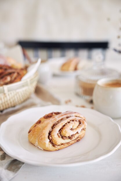 Vertikale Nahaufnahme von leckeren Nussschnecken mit Kaffee-Cappuccino auf dem weißen Holztisch