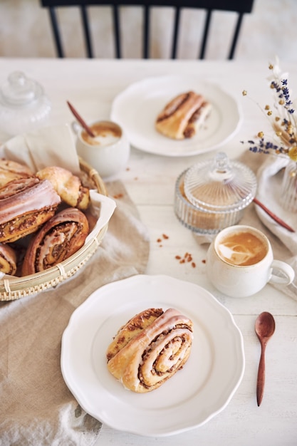 Vertikale Nahaufnahme von leckeren Nussschnecken mit Kaffee-Cappuccino auf dem weißen Holztisch