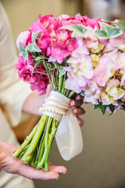 Vertikale Nahaufnahmeaufnahme der Braut, die ihren eleganten Hochzeitsstrauß mit rosa und weißen Blumen hält