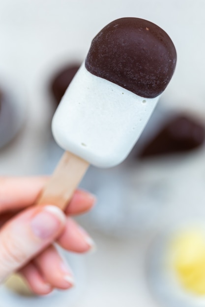 Vertikale Nahaufnahmeaufnahme einer weiblichen Hand, die ein rohes veganes Eis am Stock hält