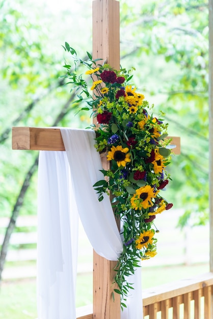 Vertikale Nahaufnahmeaufnahme eines Blumenstraußes auf einem Holzkreuz, das mit einem weißen Stoff bedeckt wird