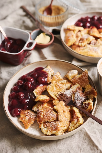 Vertikale Nahaufnahmeaufnahme von köstlichen flauschigen Pfannkuchen mit Kirsche und Puderzucker