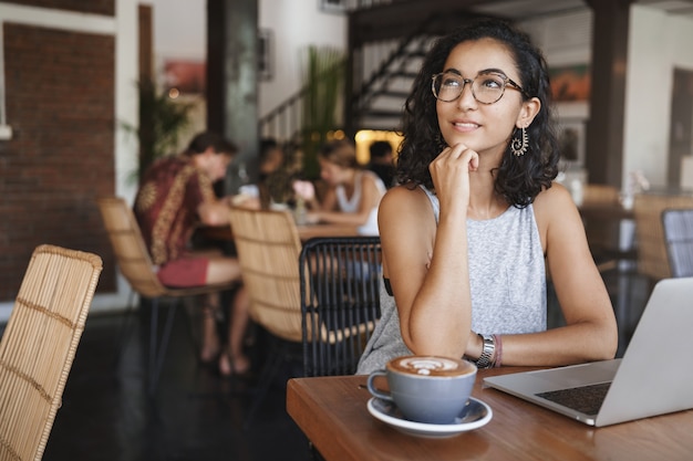 Vertikale Schuss sanfte zarte entspannte städtische Frau, die Brille trägt, genießt Moment, der allein im Café sitzt