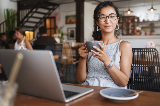 Vertikale Schuss sanfte zarte entspannte städtische Frau, die Brille trägt, genießt Moment, der allein im Café sitzt