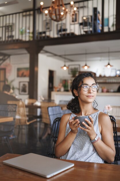 Vertikale Schuss sanfte zarte entspannte städtische Frau, die Brille trägt, genießt Moment, der allein im Café sitzt