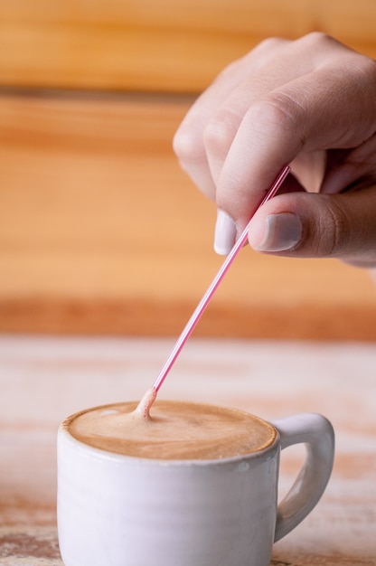 Vertikale selektive Fokusaufnahme einer Person, die einen Stock in eine Tasse Kaffee setzt