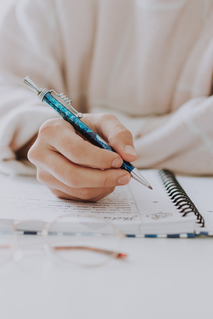 Kostenlose Foto vertikale selektive nahaufnahme einer weiblichen schrift in einem notizbuch mit einem blauen stift