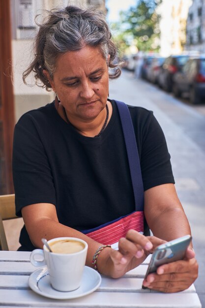 Vertikaler flacher Fokus einer Frau, die ihr Telefon auf dem Tisch im Freien eines Cafés benutzt