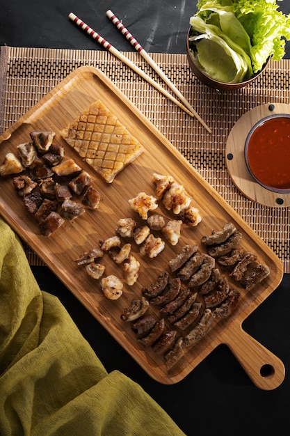 Vertikaler Hochwinkelschuss einer Holzplatte, die mit geröstetem Essen auf einer schwarzen Oberfläche gefüllt ist