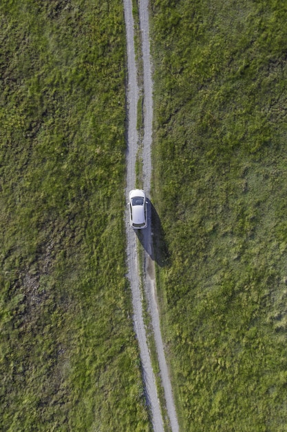 Vertikaler Hochwinkelschuss eines weißen Autos, das durch den Weg im grünen Tal reitet