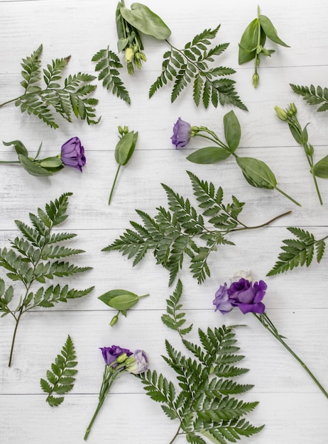 Kostenloses Foto vertikaler hochwinkelschuss von lila lisianthusblumen und grünen blättern auf einer holzoberfläche
