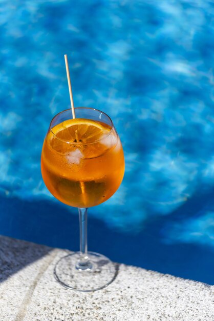 Vertikaler Schuss aus einem Glas Saft mit einer Orangenscheibe, isoliert am Pool in Algarve Portugal