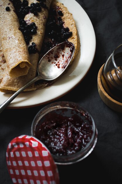 Vertikaler Schuss des hohen Winkels von köstlichen Crepes mit Blaubeermarmelade auf einer schwarzen Oberfläche