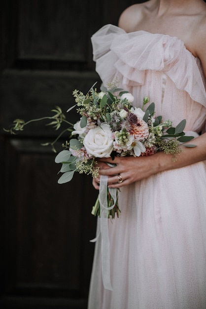 Vertikaler Schuss einer Braut, die Hochzeitskleid trägt, das einen Blumenstrauß hält