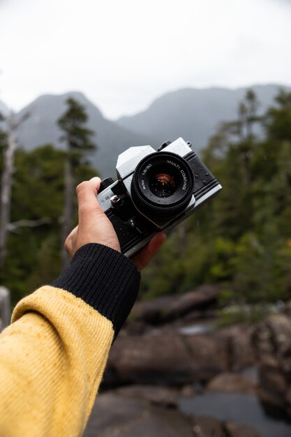 Vertikaler Schuss einer männlichen Hand, die eine professionelle Fotokamera mit Wald auf hält