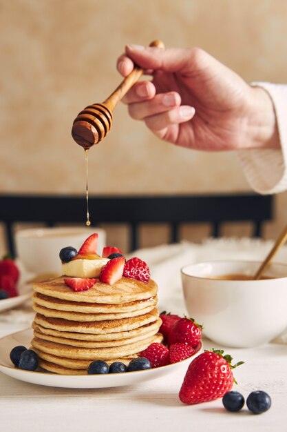 Vertikaler Schuss einer Person, die Sirup auf die veganen Pfannkuchen mit Früchten setzt