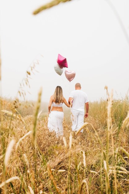 Vertikaler Schuss eines kaukasischen Paares, das herzförmige Luftballons im Feld hält