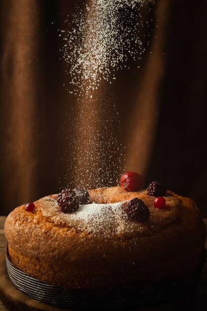 Vertikaler Schuss eines köstlichen Kuchens mit Puderzucker, roten Beeren, Erdbeeren und Brombeeren