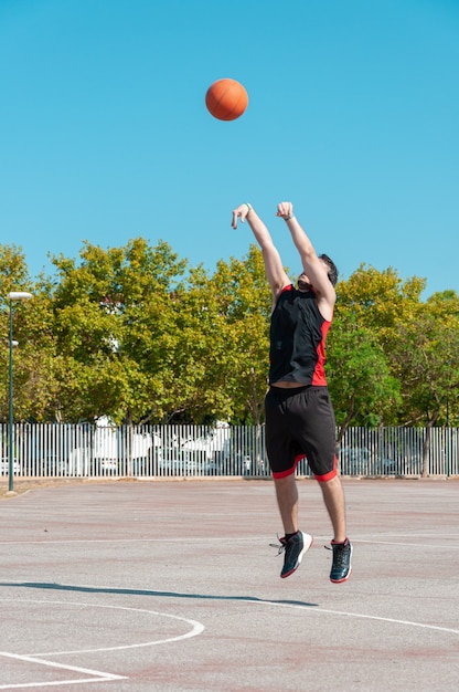 Vertikaler Schuss eines Mannes, der den Basketballball in ein Gericht wirft