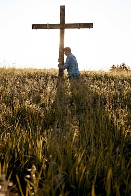 Vertikaler Schuss eines Mannes mit seinem Kopf gegen ein Holzkreuz in einem Grasfeld