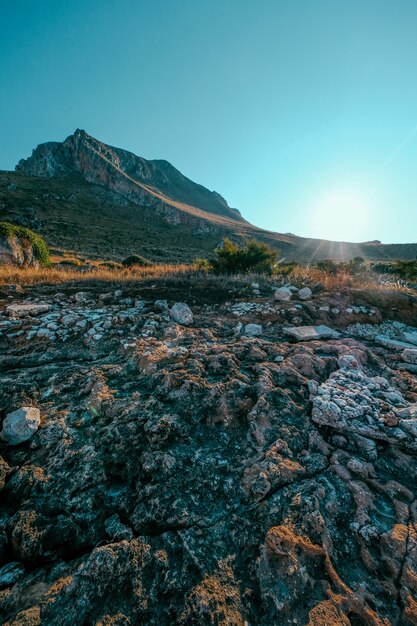 Vertikaler Schuss von Felsen nahe einem trockenen Grasfeld mit Berg und einem klaren blauen Himmel