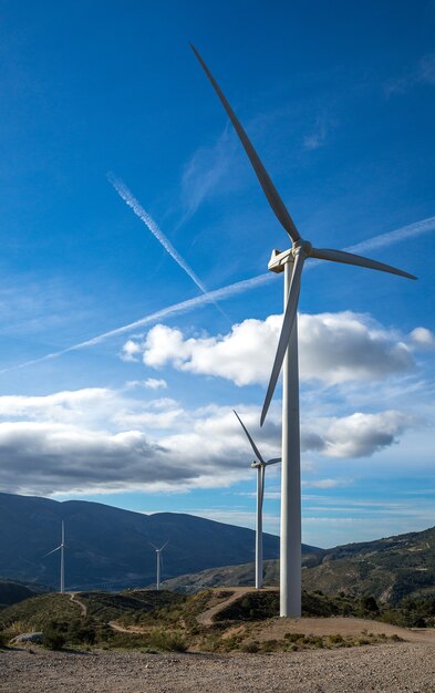 Vertikaler Schuss von mehreren weißen elektrischen Windmühlen auf einem Hügel