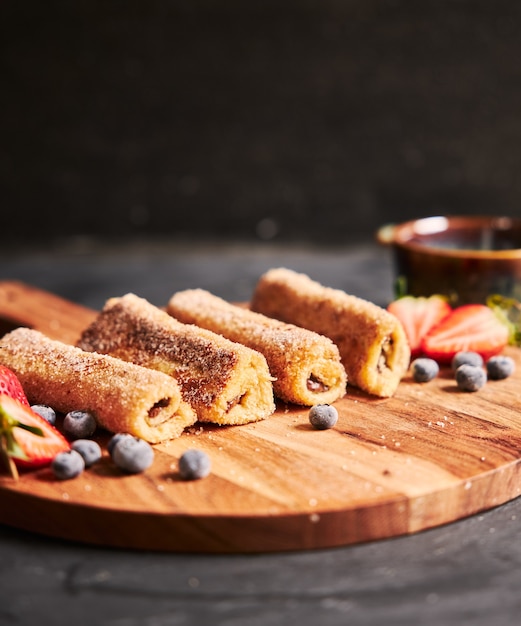 Vertikaler Schuss von Toastrollen mit Beeren auf einem Holzteller mit einem schwarzen Hintergrund