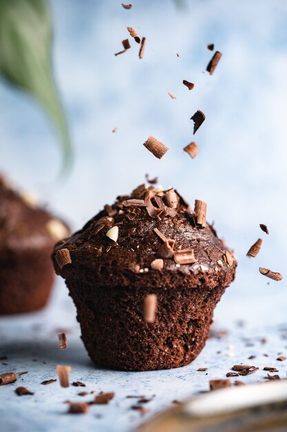 Vertikaler selektiver Fokusschuss von Schokoladencupcakes auf einer blauen Oberfläche mit fallenden Schokoladenstückchen