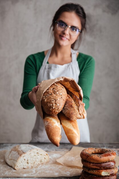 Vertikales Bild des weiblichen Bäckers, der Tasche mit Brot zeigt