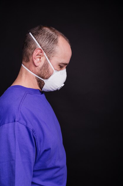 Vertikales Bild eines Mannes mit einer Gesichtsmaske vor einem dunklen Hintergrund - COVID-19