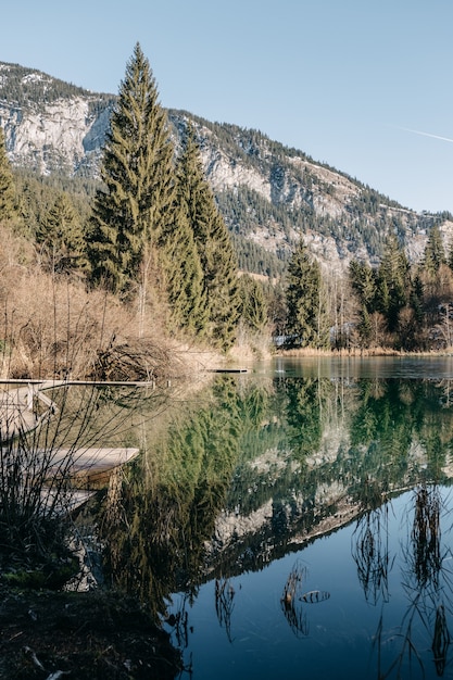 Vertikales Bild eines Sees, umgeben von Felsen und Wäldern mit Bäumen, die auf dem Wasser reflektieren