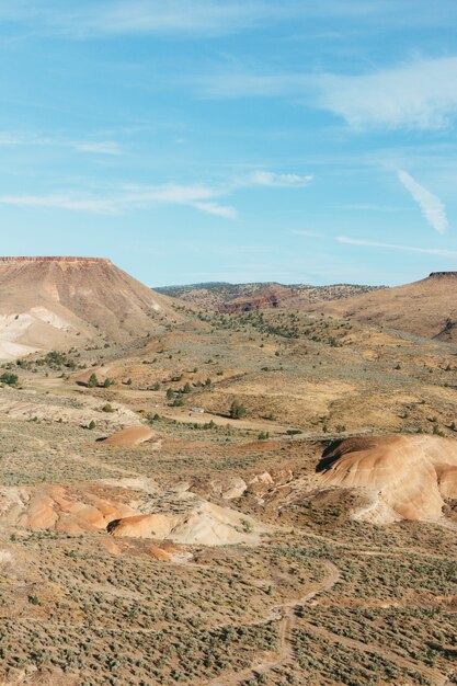 Vertikales Bild von Felsen bedeckt mit Sand und Grün unter Sonnenlicht und einem blauen Himmel