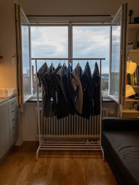 Vertikales Bild von Kleidung, die auf einem Metallgestell gegen ein offenes Fenster trocknet
