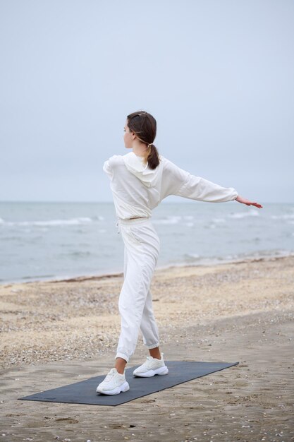 Vertikales Foto einer jungen Dame, die am Strand steht und ihren Körper streckt Foto in hoher Qualität