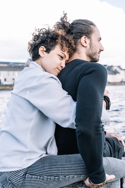 Vertikales Foto eines Mädchens, das zurück ihren Partner mit dem Meer unscharf umarmt